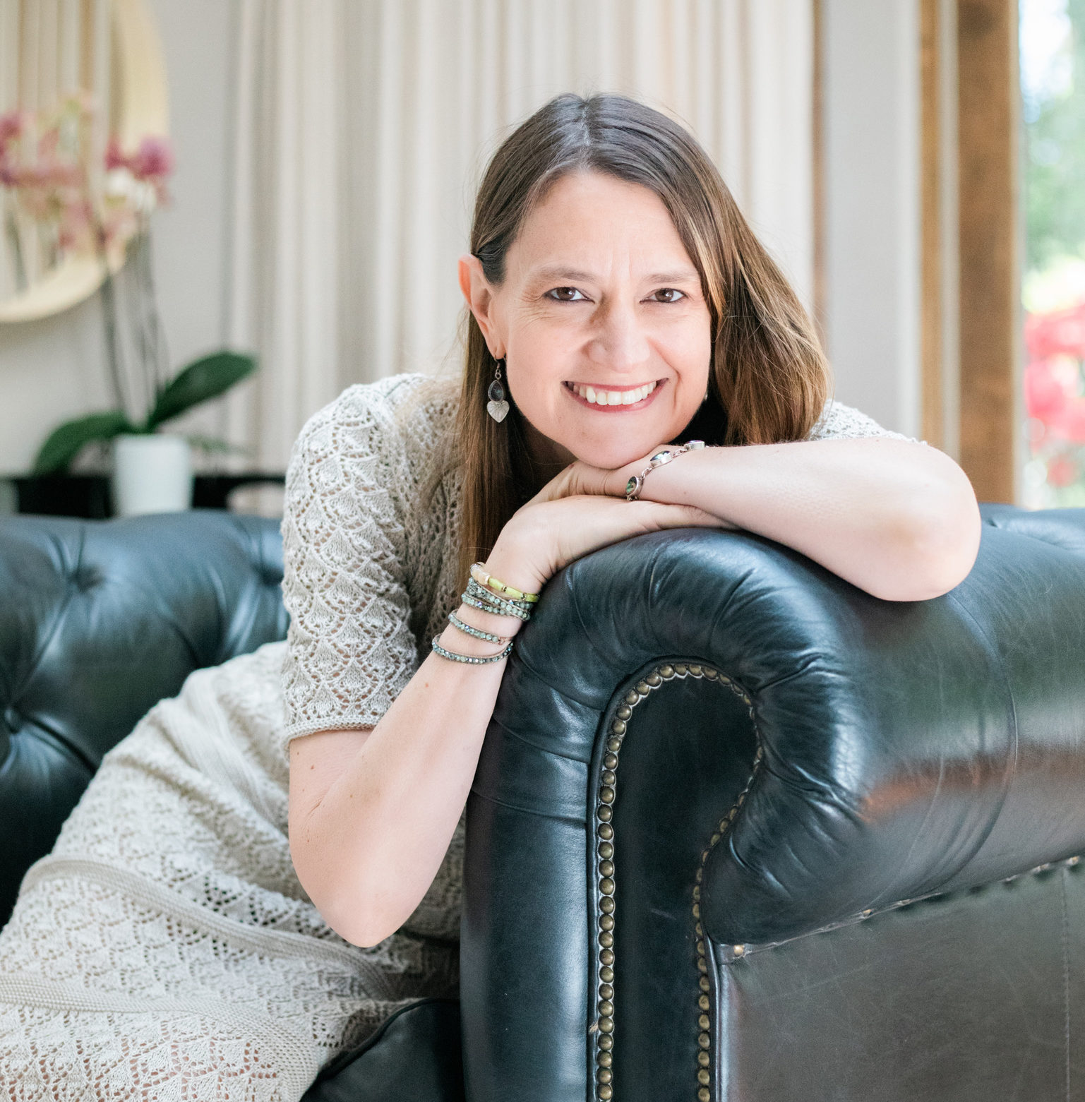 Woman leans on a sofa, adorned with bracelets, in a reflective pause